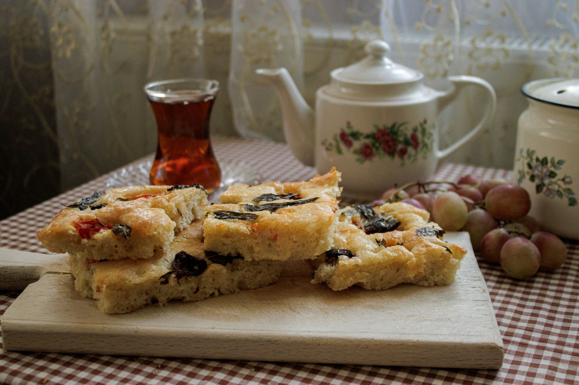 Rustykalna domowa focaccia na desce obok herbaty i winogron