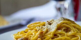 Spaghetti carbonara z tartym parmezanem na białym talerzu