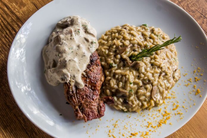 Stek z sosem podany z kremowym risotto grzybowym na talerzu Stek z sosem podany z kremowym risotto grzybowym na talerzu