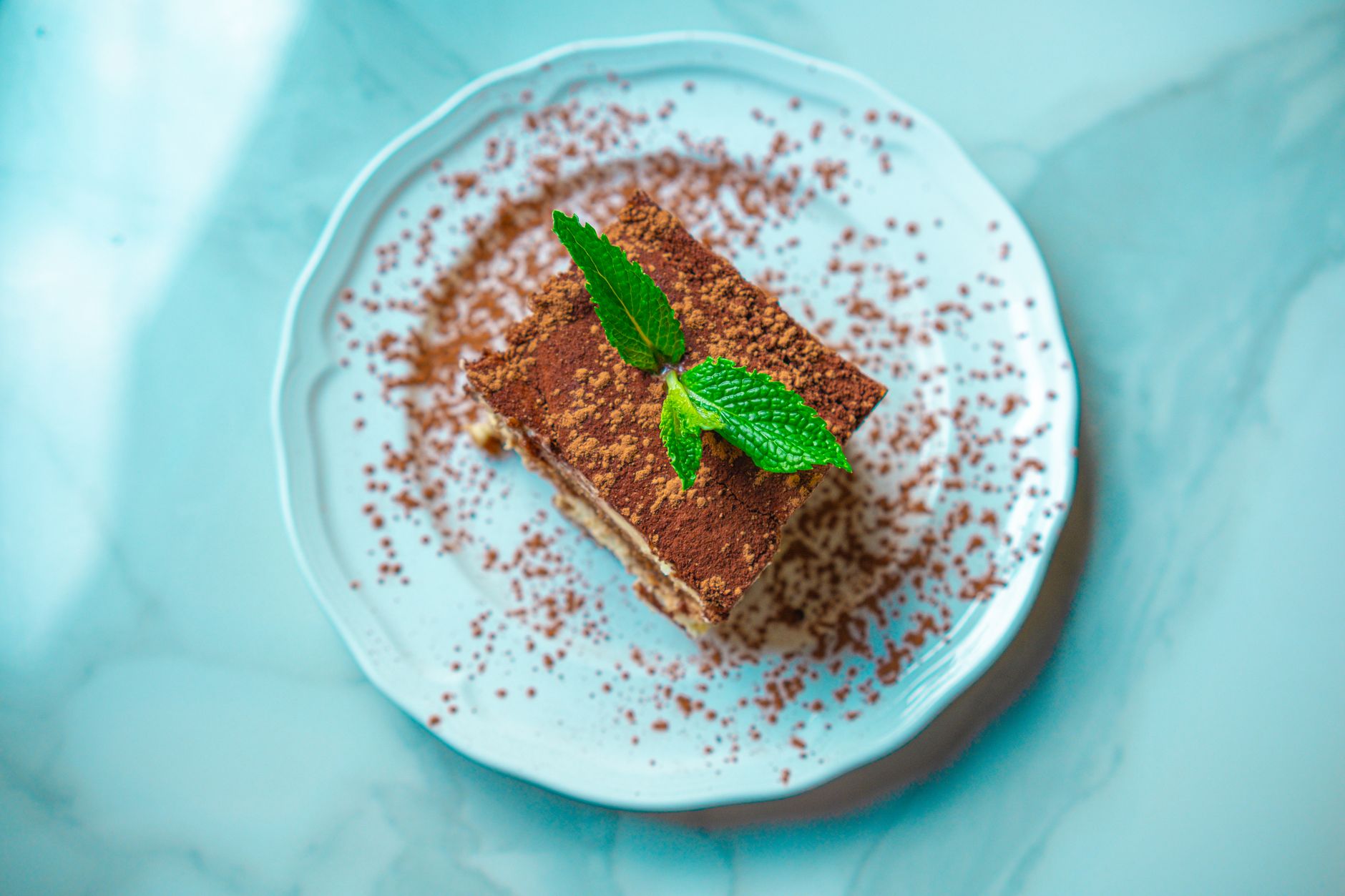 Kawałek tiramisu z listkiem mięty na marmurowym talerzu